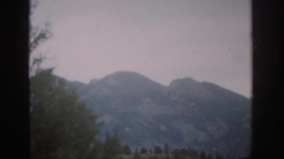 1959 Colorado mountain landscape filmed through a dark frame, with foreground trees and soft, faded 8mm color.