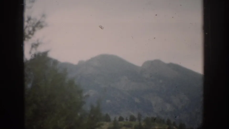 1959 Colorado 8mm frame showing a soft mountain slope, foreground foliage, and dark framing at the edge of the view.