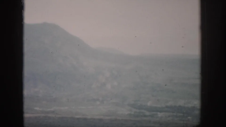 1959 Colorado 8mm view of a hazy valley below a mountain slope, framed by dark edges and faded mid-century film color.