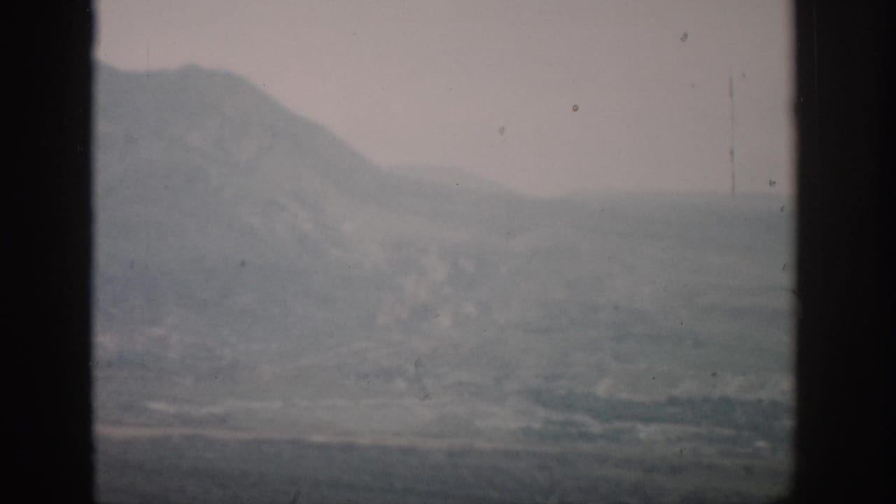 1959 Colorado home-movie frame showing distant hazy mountains and a muted plain divided by dark window bars.