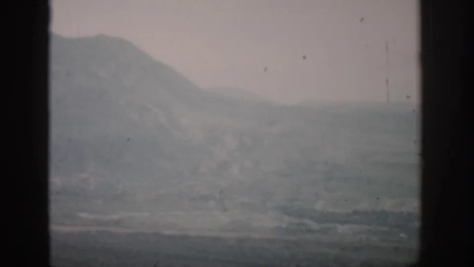 1959 Colorado home-movie frame showing distant hazy mountains and a muted plain divided by dark window bars.