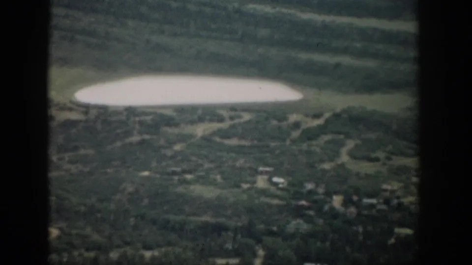 Clearer 1959 Colorado valley view showing an oval lake, grassy fields, roads, and small buildings beyond the window frame.