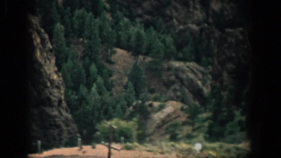 1959 Colorado 8mm frame of a rocky evergreen hillside, softened by film grain and warm faded color.