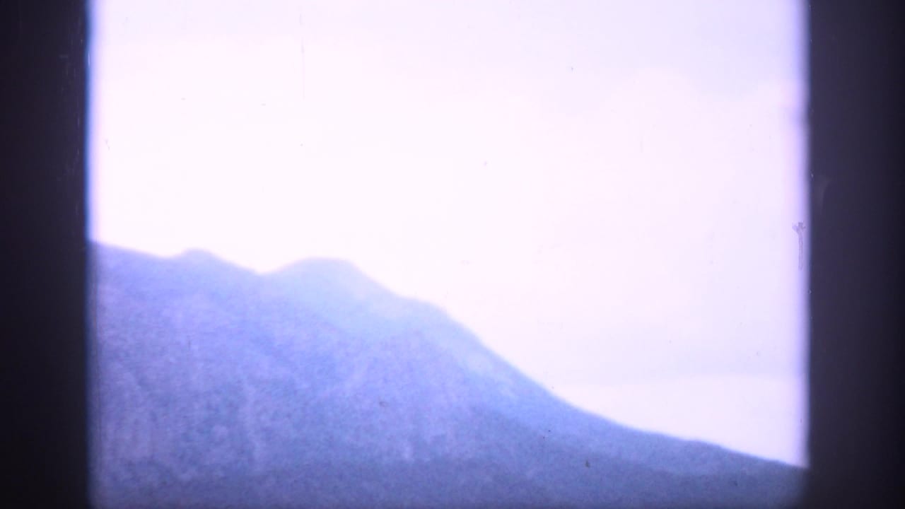 1959 Colorado 8mm view of a hazy mountain ridge under pale blue-violet sky through a dark divided frame.