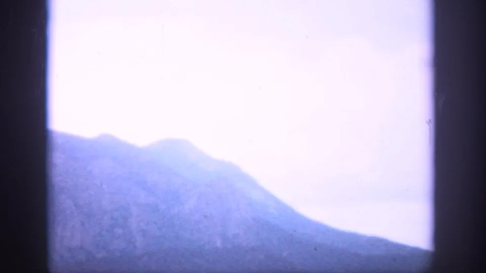 1959 Colorado 8mm view of a hazy mountain ridge under pale blue-violet sky through a dark divided frame.