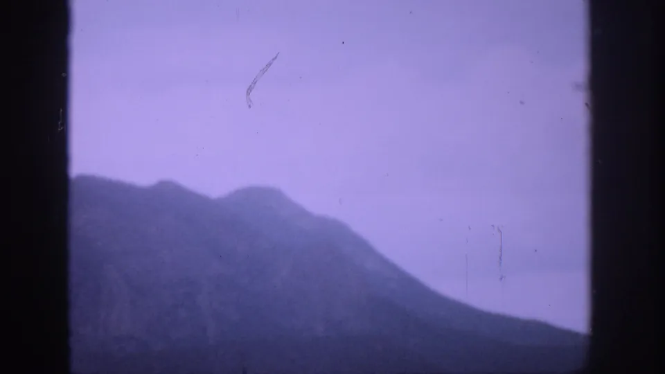1959 Colorado 8mm frame with a dark mountain ridge, violet-tinted sky, visible film scratches, and a vertical divider.