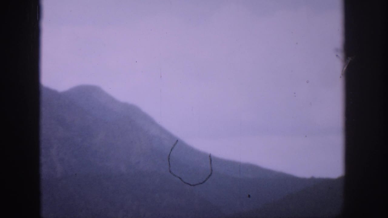 1959 Colorado 8mm frame showing a hazy mountain slope through a dark window frame, with a pale purple sky and visible film wear.