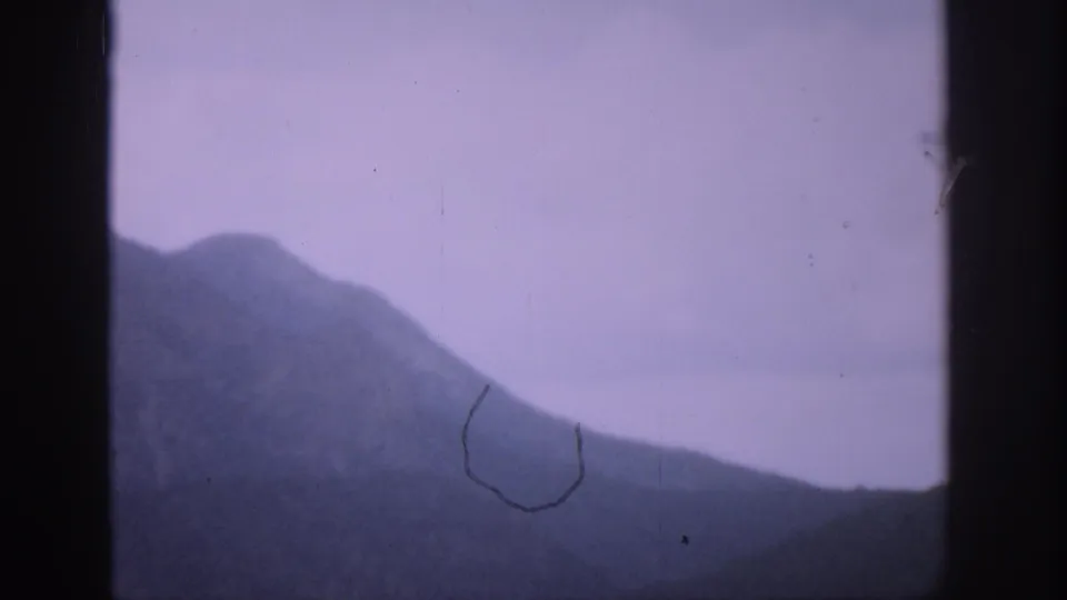 1959 Colorado 8mm frame showing a hazy mountain slope through a dark window frame, with a pale purple sky and visible film wear.
