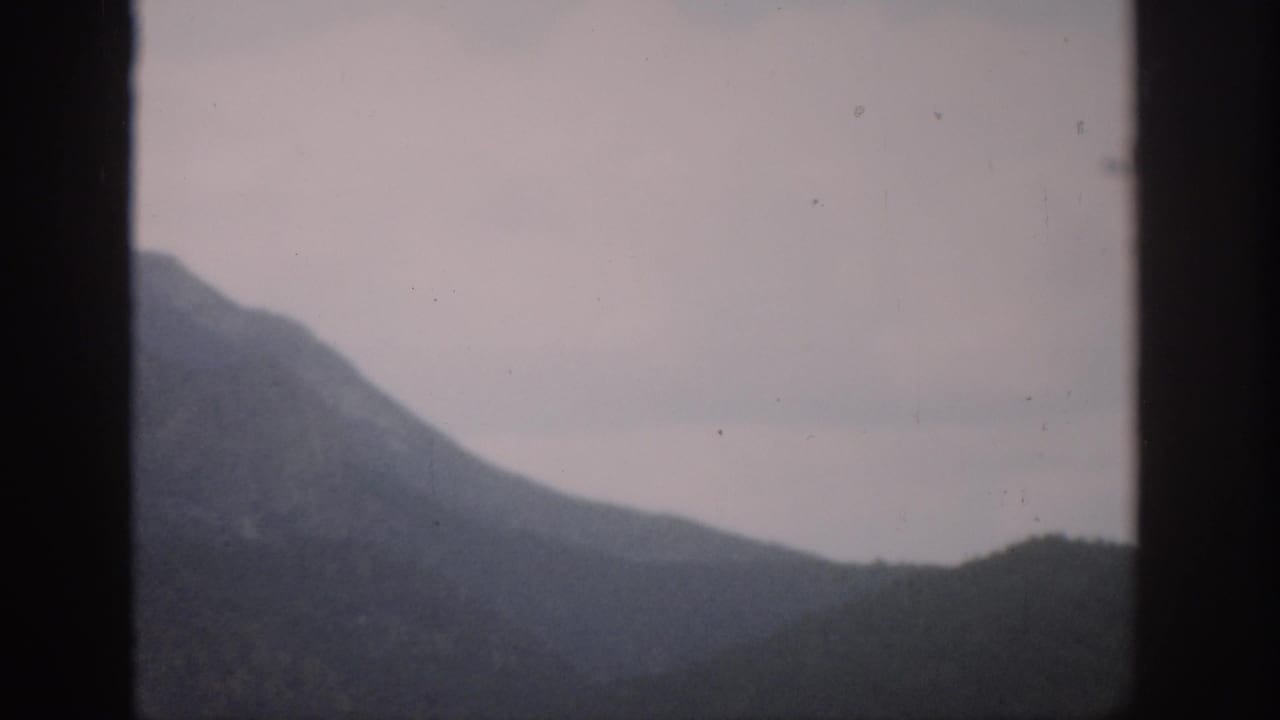 Distant mountain and lower hills framed by dark vertical window bars under an overcast sky.