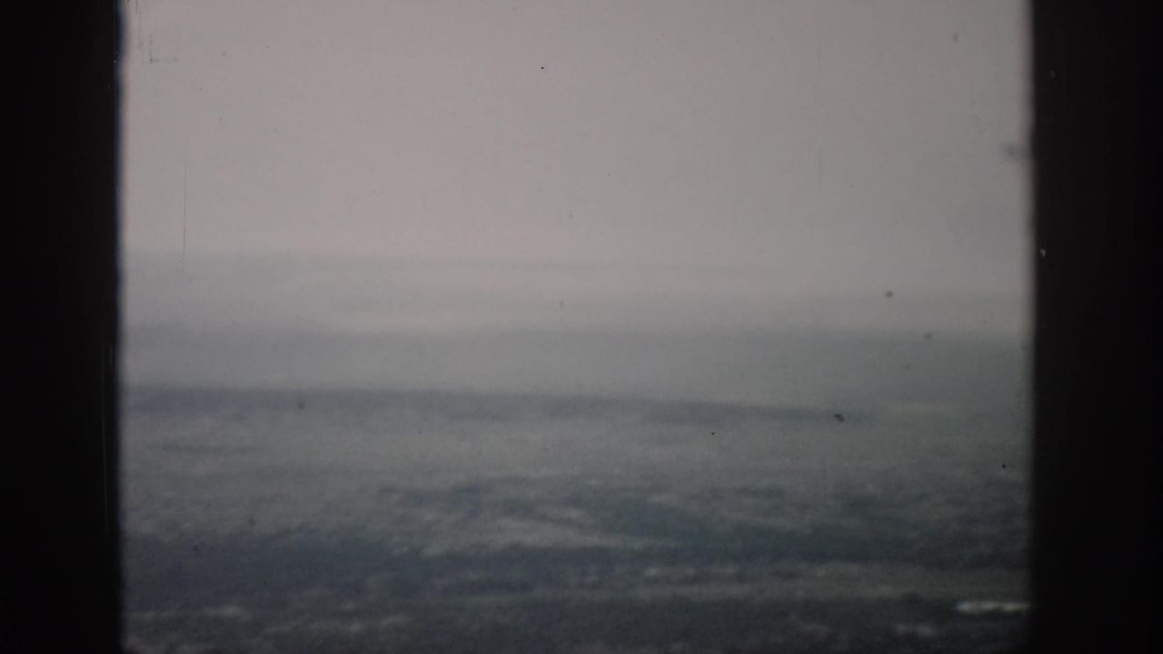 1959 Colorado 8mm frame showing a muted aerial landscape through an airplane window with dust and soft film grain.