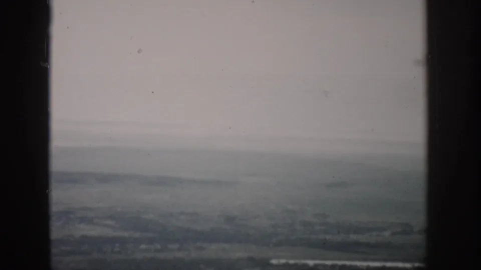 The airplane-window view shows a hazy Colorado landscape below, with faint field patterns and visible dust on the 8mm scan.