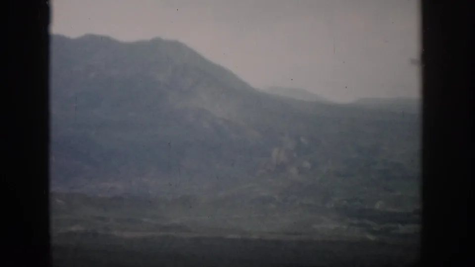 1959 Colorado 8mm frame with hazy mountain slopes and valley terrain viewed through a window.