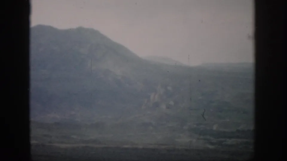 1959 Colorado home-movie frame showing a softened mountain silhouette and valley floor in haze.