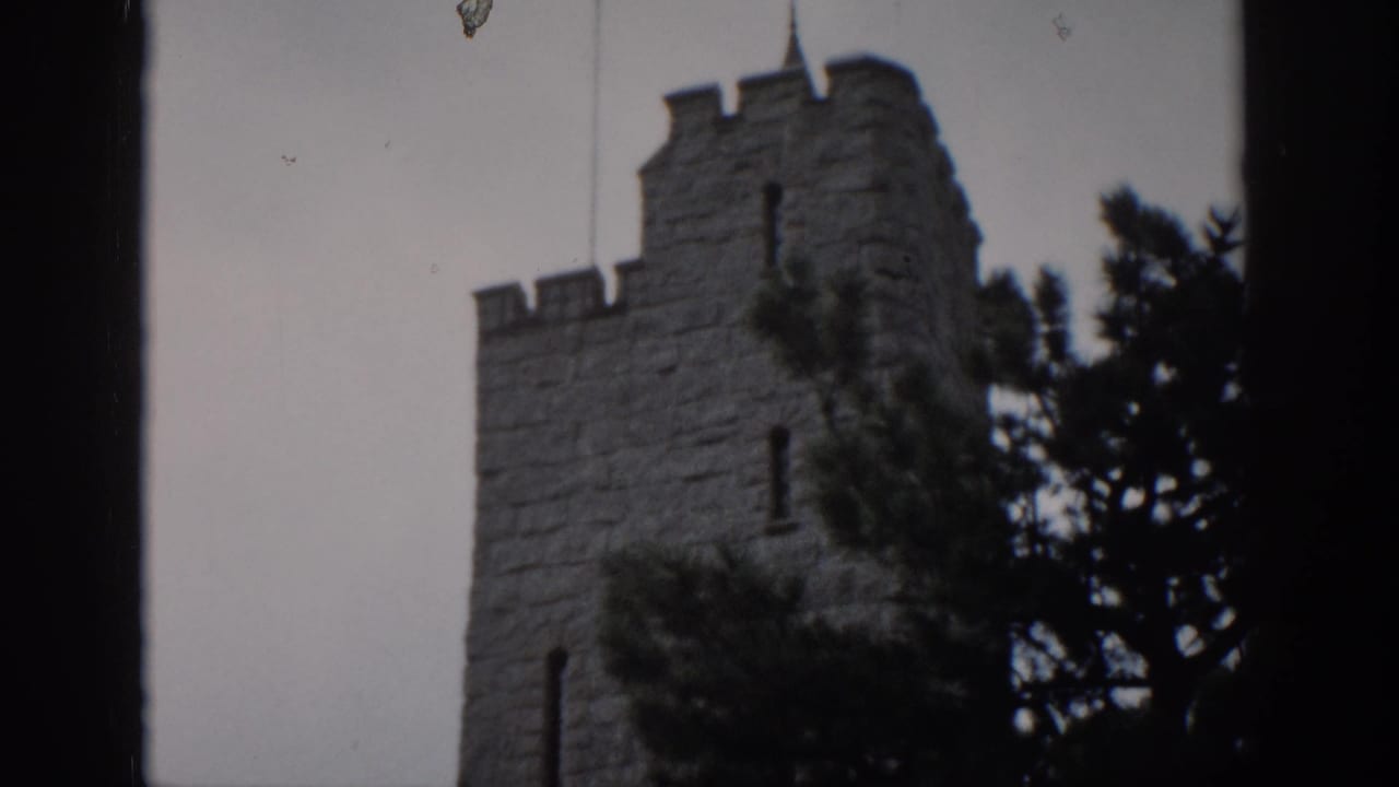 1959 Colorado 8mm frame showing a castle-like stone tower with battlements, trees, gray sky, and dark framing at the edges.