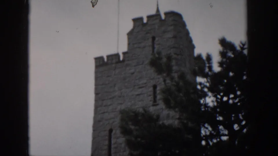 1959 Colorado 8mm frame showing a castle-like stone tower with battlements, trees, gray sky, and dark framing at the edges.