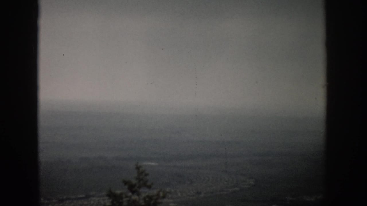 1959 Colorado 8mm view over a hazy valley landscape, framed by dark vertical edges and softened by overcast light.