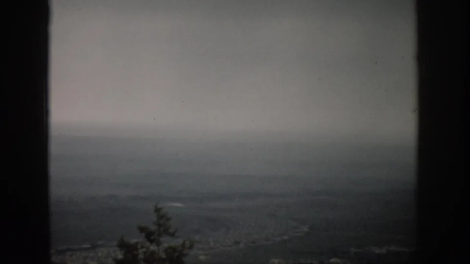 1959 Colorado 8mm overlook frame showing a muted, foggy valley and distant terrain with a small tree shape at the lower edge.