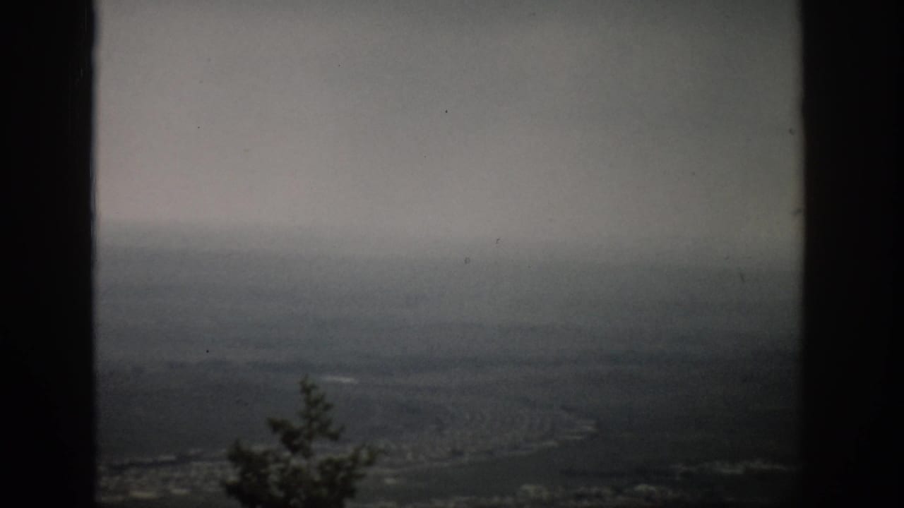 1959 Colorado 8mm frame showing a hazy plain with a faint winding line, dark framing edges, and fog-softened distance.