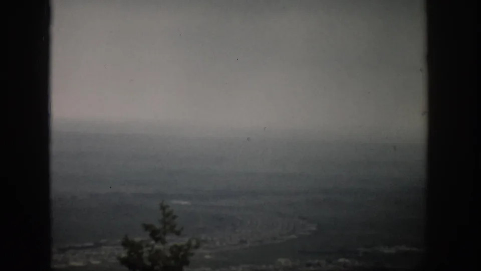 1959 Colorado 8mm frame showing a hazy plain with a faint winding line, dark framing edges, and fog-softened distance.