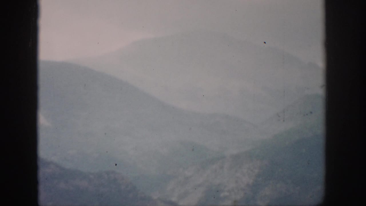 1959 Colorado home-movie frame with blue-gray mountain ridges receding into mist and a pale, softly exposed sky.