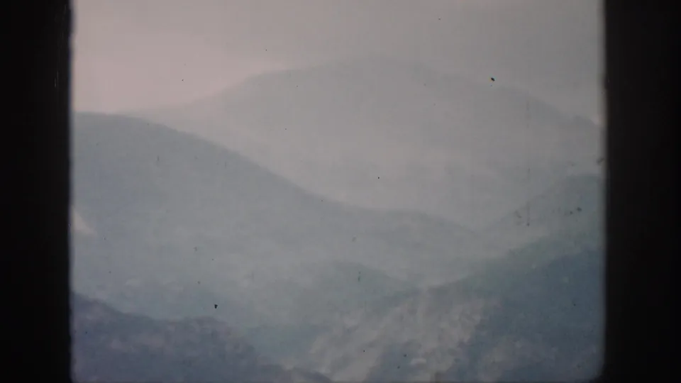 1959 Colorado home-movie frame with blue-gray mountain ridges receding into mist and a pale, softly exposed sky.