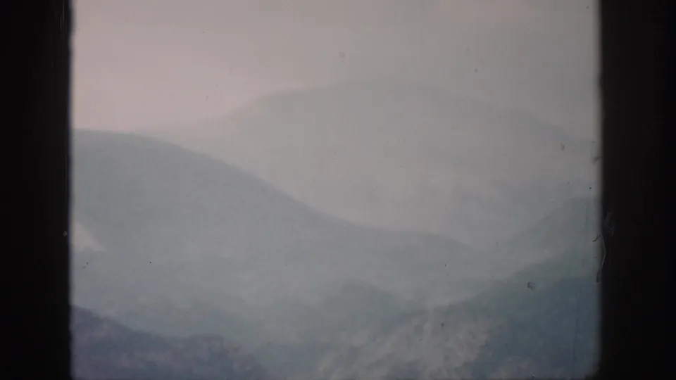 1959 Colorado 8mm frame showing fog-dipped mountain ridges, subdued color, and dark film or window borders at the sides.
