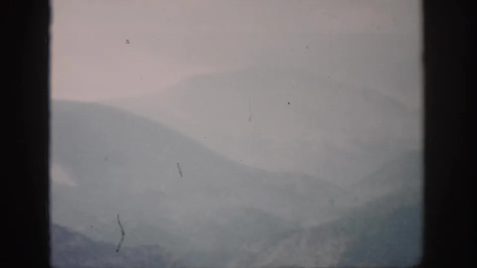 1959 Colorado home-movie frame with misty mountain layers and a vertical window bar in the foreground.