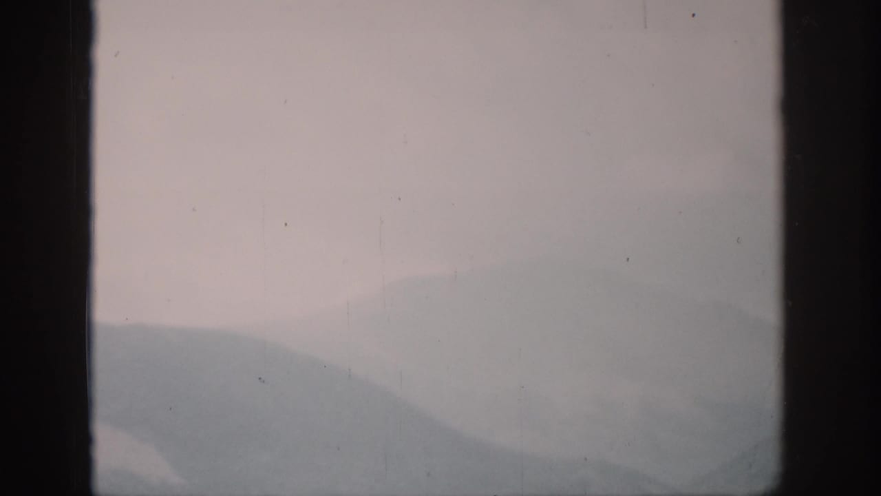 1959 Colorado 8mm frame showing hazy mountain ridges at dawn through dark vertical window framing.