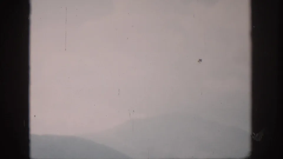 1959 Colorado 8mm still with a low hazy ridge, pale sky, dark frame edges, and visible film dust.