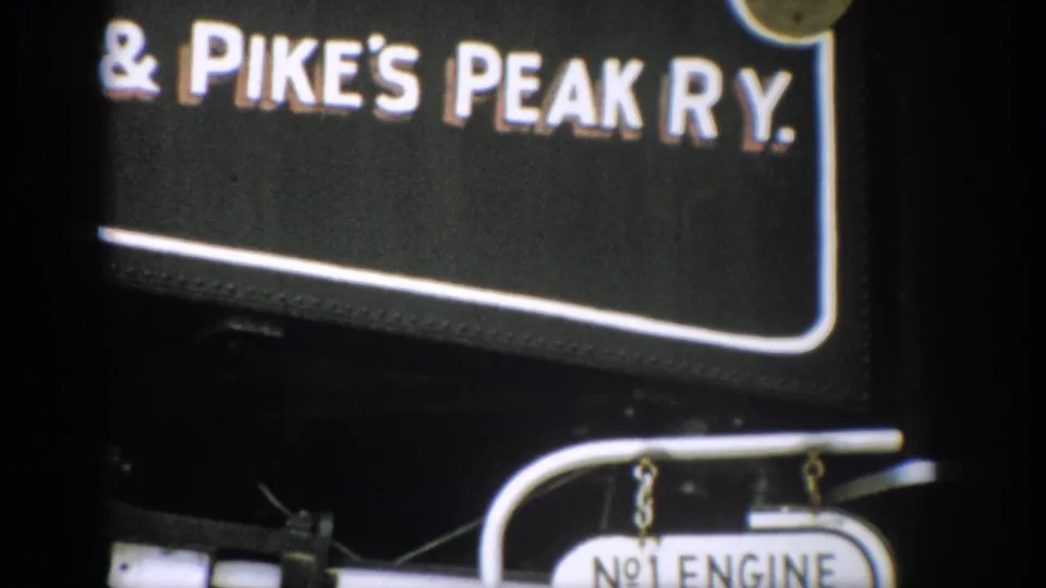 1959 home-movie frame showing cropped Pike's Peak Ry. lettering, a No.1 Engine plate, and nearby rail hardware.