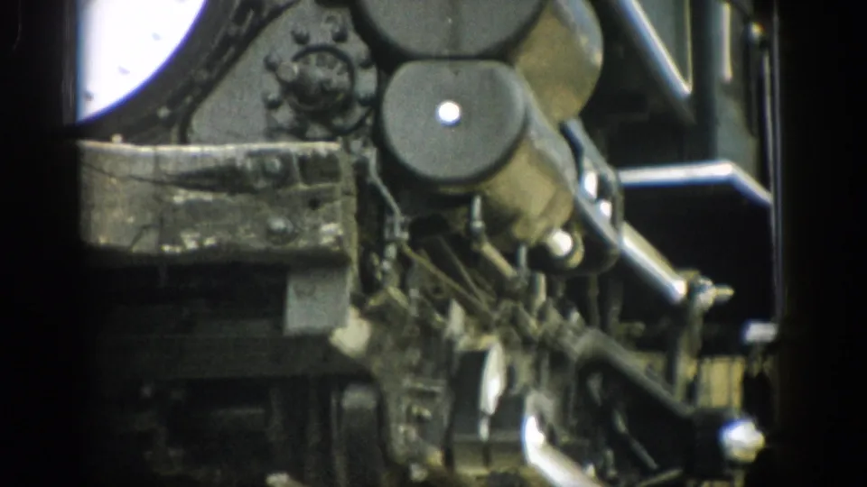 Handheld 8mm frame of 1959 Colorado steam train mechanics, showing rods, circular housings, and a dark side structure.