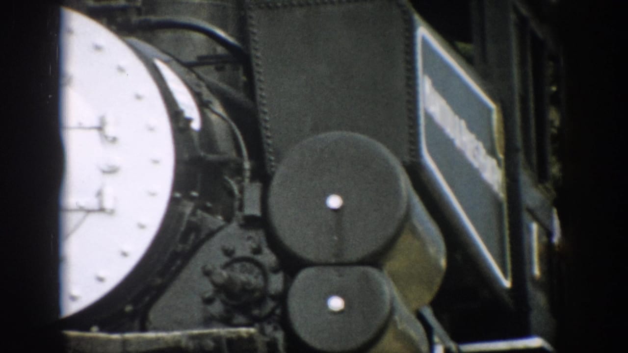 Close view of a black steam locomotive with a white front plate and side machinery.