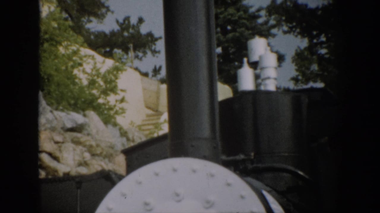 1959 Colorado 8mm frame showing close locomotive details framed by dark train-window edges, with trees and rock slope behind.