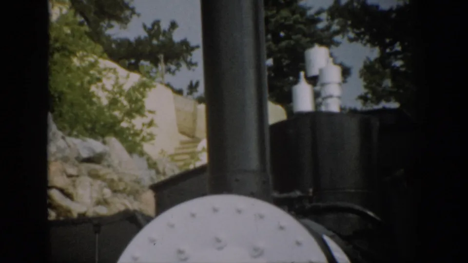 1959 Colorado 8mm frame showing close locomotive details framed by dark train-window edges, with trees and rock slope behind.