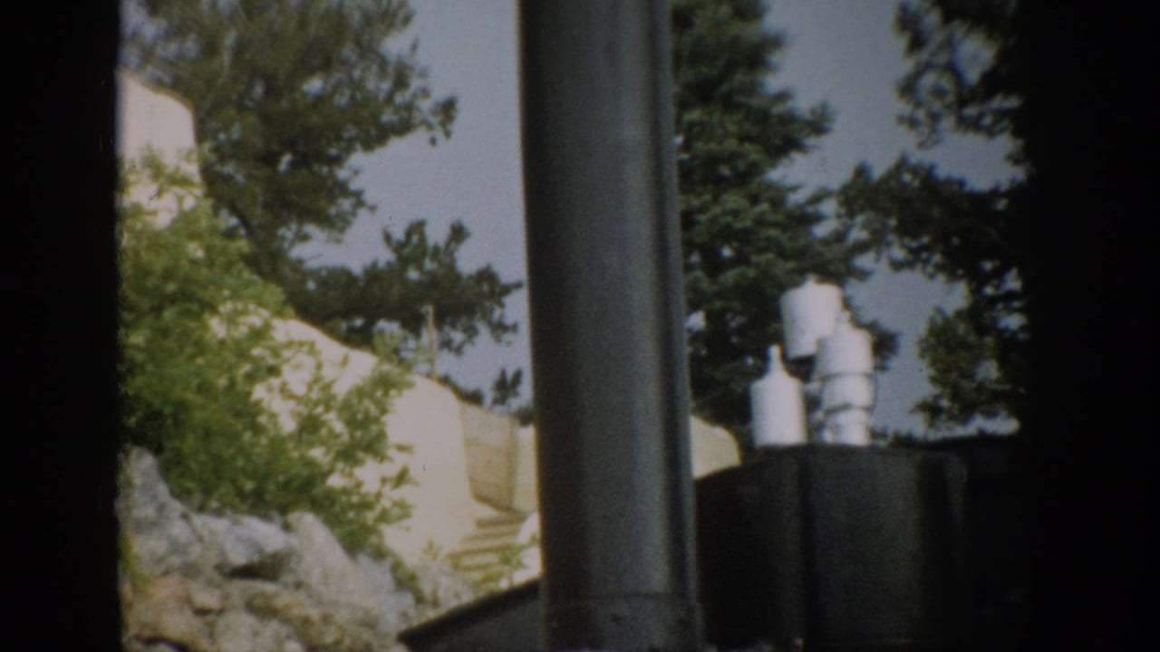 1959 Colorado train-view frame with dark locomotive equipment in the foreground and wooded hillside scenery beyond.