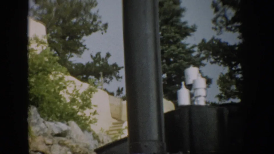 1959 Colorado train-view frame with dark locomotive equipment in the foreground and wooded hillside scenery beyond.