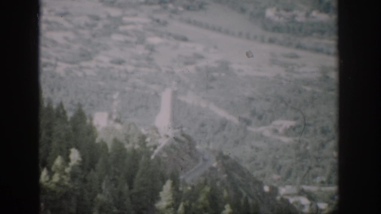 1959 Colorado 8mm frame showing a hazy mountain valley, winding road, scattered structures, and dark film borders.