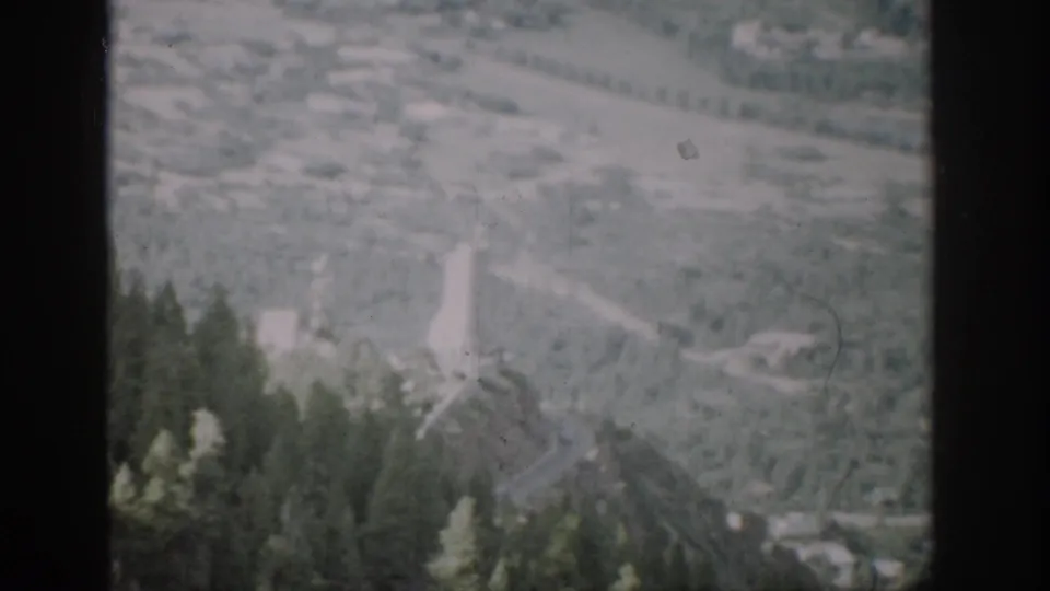 1959 Colorado 8mm frame showing a hazy mountain valley, winding road, scattered structures, and dark film borders.