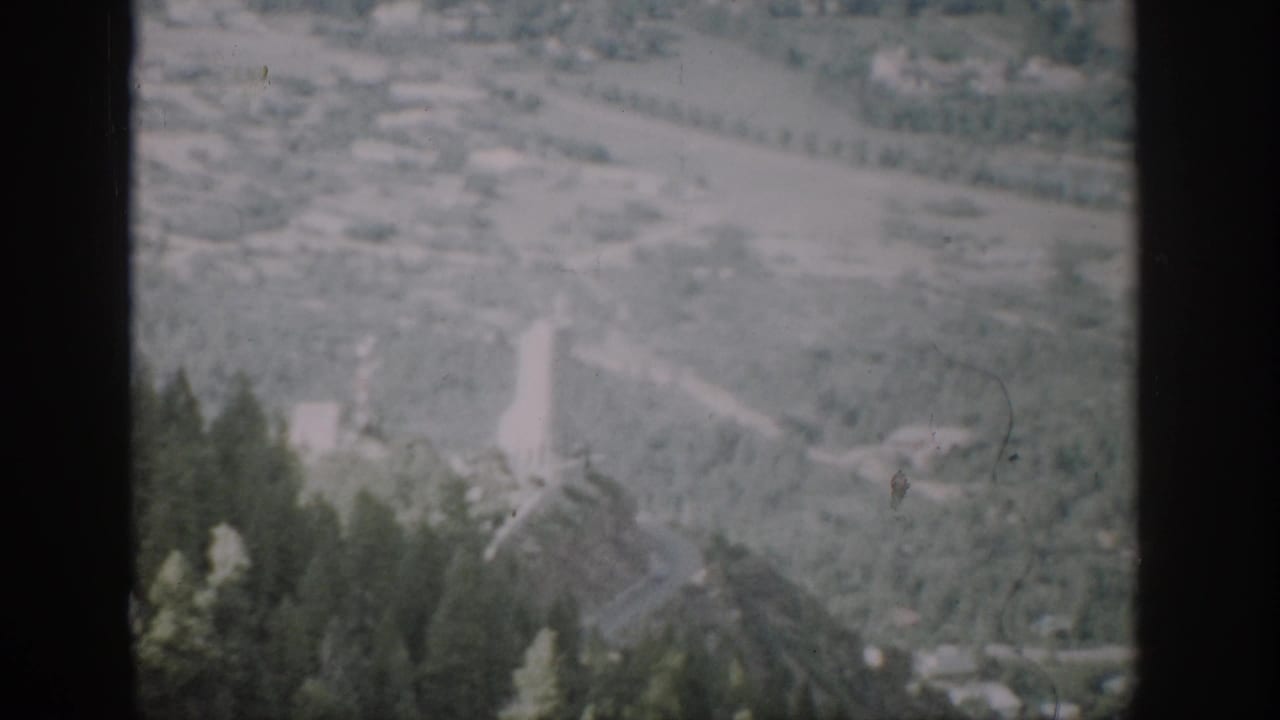 Mountain valley and road seen beyond dark film dividers and evergreen trees.