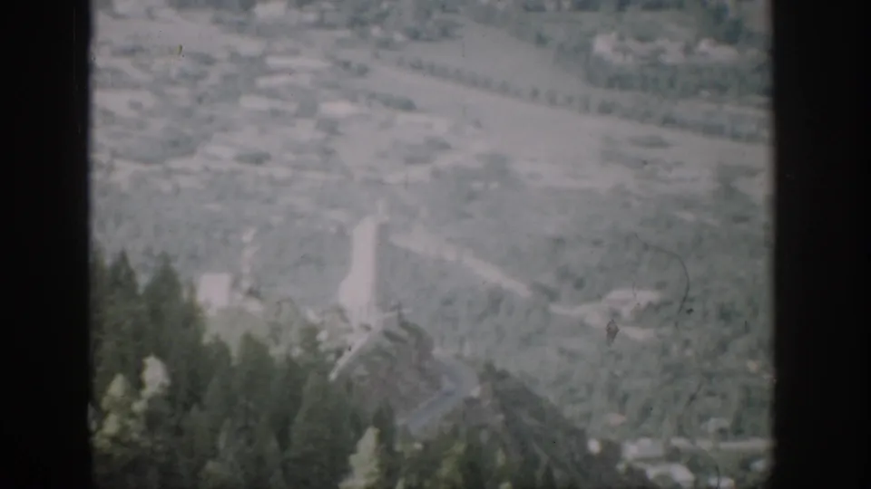Colorado mountain valley view on 8mm film, with a pale road, forested foreground, scattered buildings, and scan artifacts.