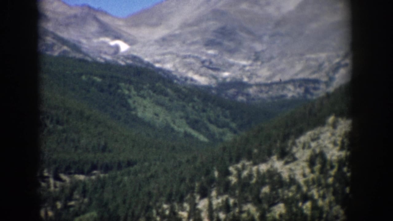 Colorado mountain panorama with conifer forest, rocky ridges, and a small high snow patch in 8mm color footage.
