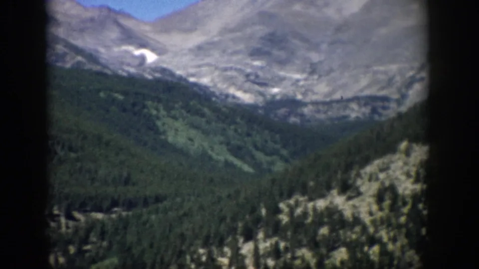 Colorado mountain panorama with conifer forest, rocky ridges, and a small high snow patch in 8mm color footage.