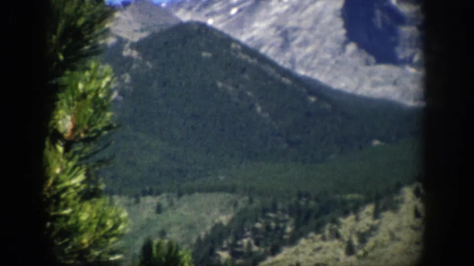 Colorado mountain landscape with evergreen branches in the foreground, forested slopes, gray rock, and small snow patches.