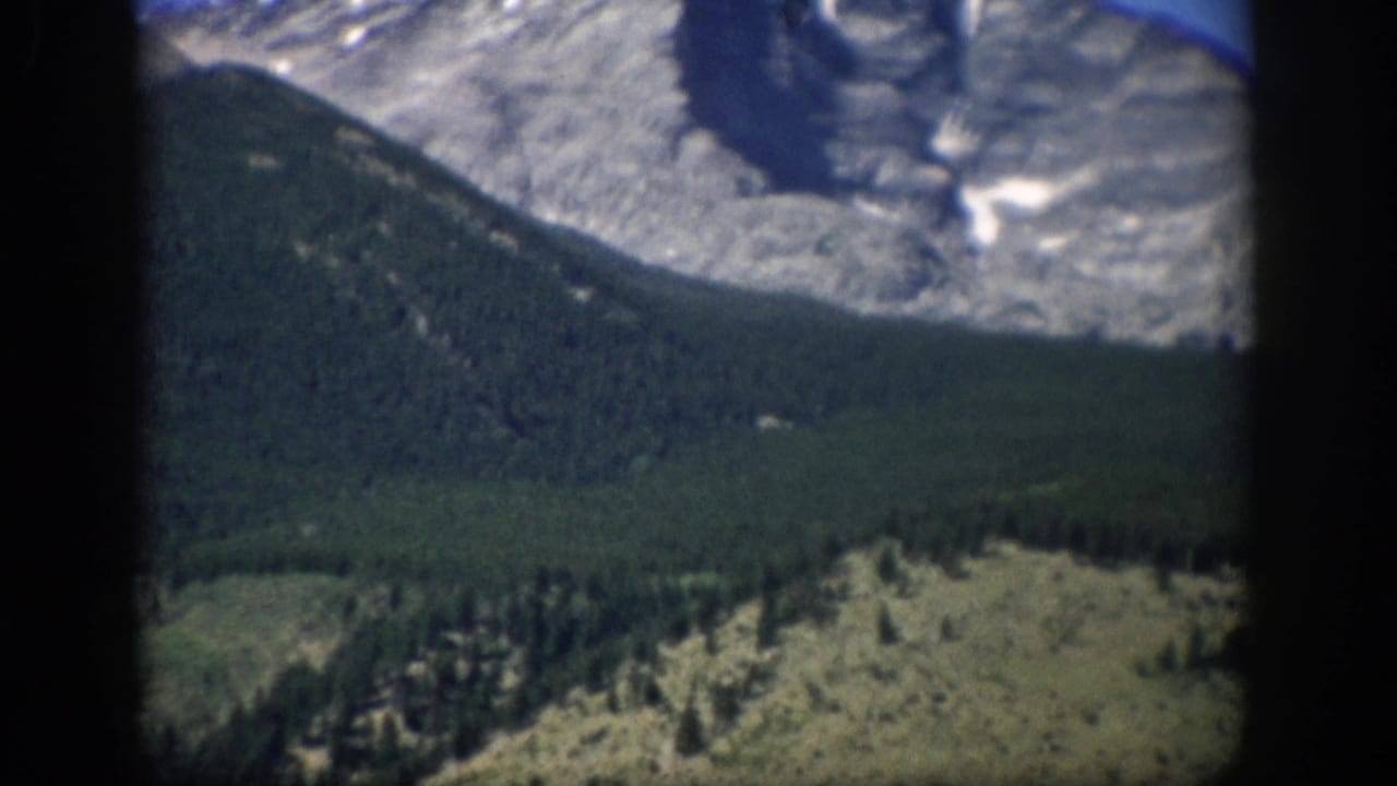 1959 Colorado 8mm frame showing a pale mountain peak, dark forested ridge, and rocky hillside within projector borders.