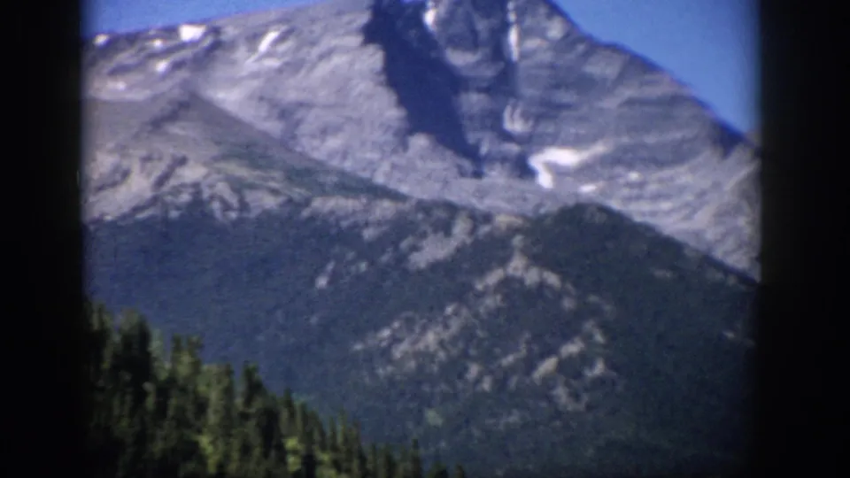 Colorado 1959 8mm frame showing gray mountain slopes, small snow traces, evergreen forest, and visible film-gate borders.