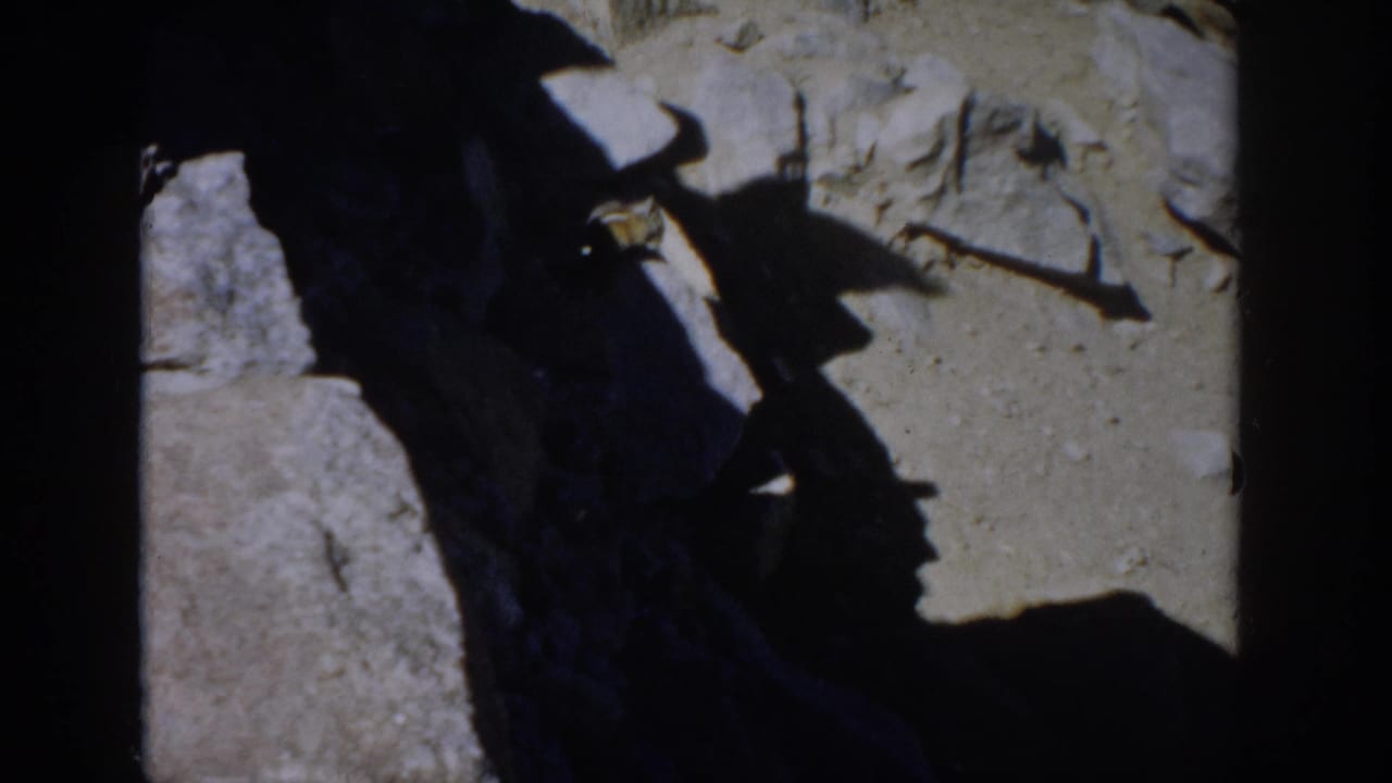 A small chipmunk is partly visible near rocks and sunlit dirt in a Colorado mountain home-movie frame.