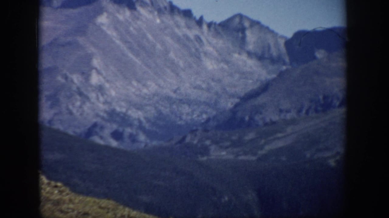 1959 Colorado 8mm view of rugged mountain ridges, shadowed valley slopes, and blue sky framed by dark edges.