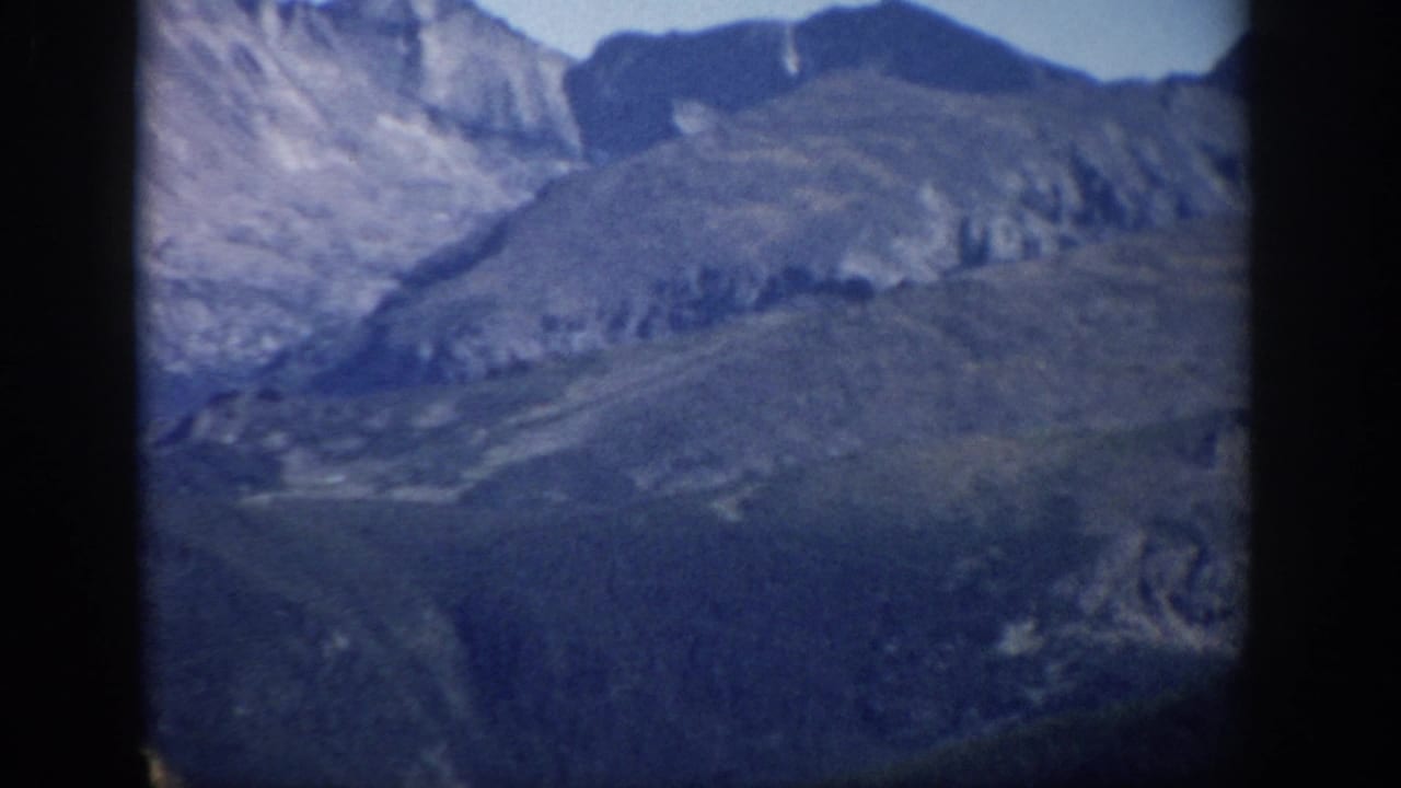 Layered rocky peaks and sloping mountain terrain under a clear sky.