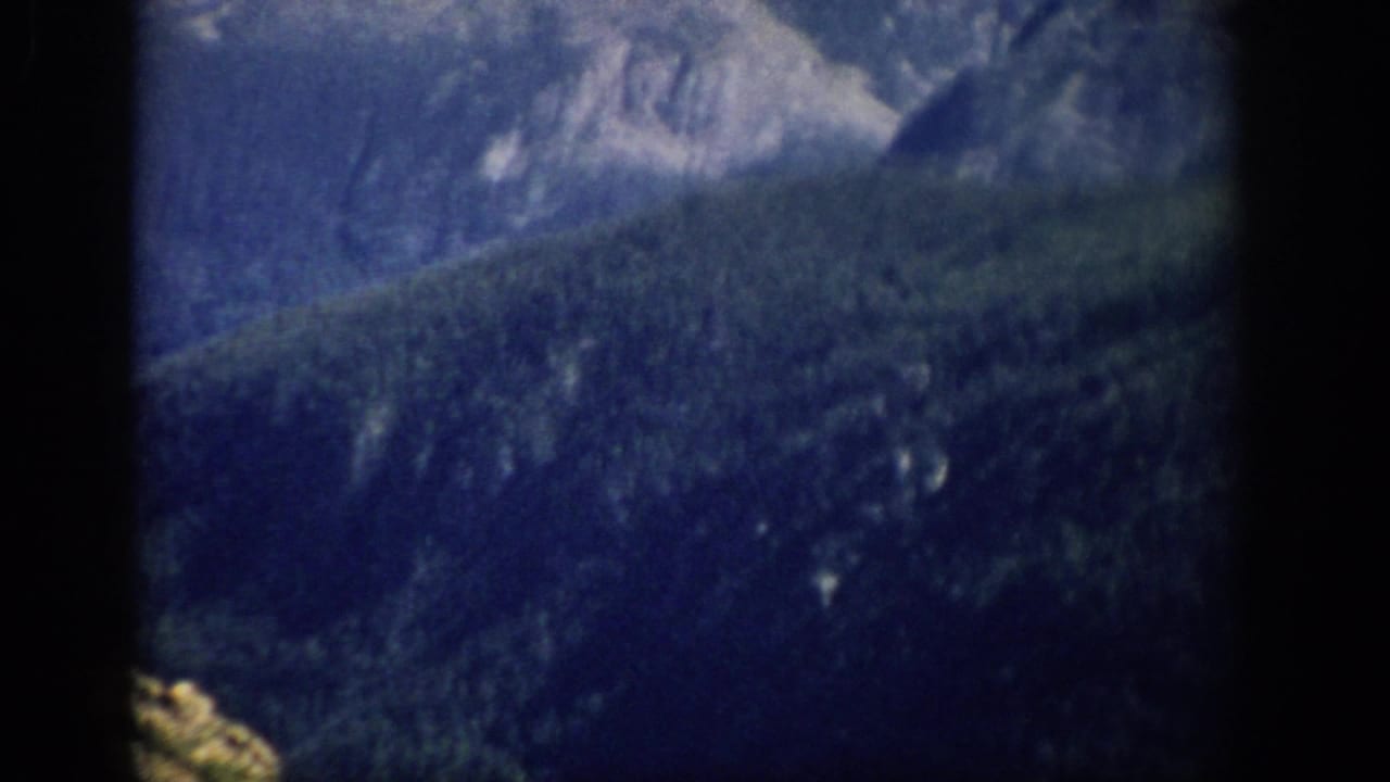 1959 Colorado 8mm frame showing distant forested mountain slopes under a pale blue sky with heavy vignette at the edges.