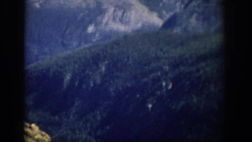 1959 Colorado 8mm frame showing distant forested mountain slopes under a pale blue sky with heavy vignette at the edges.